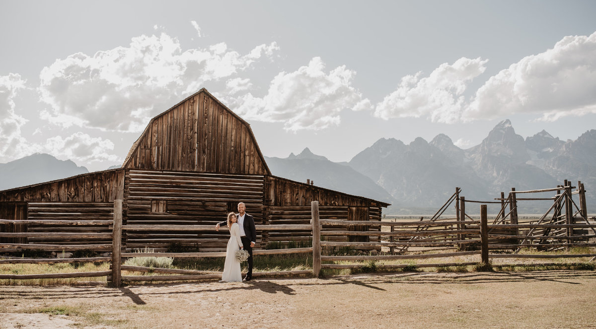 grand teton wedding with Old barn in the Tetons with a bride and her groom embracing each other on the dirt path in front of the building for their wedding pictures with jackson wyoming photographer