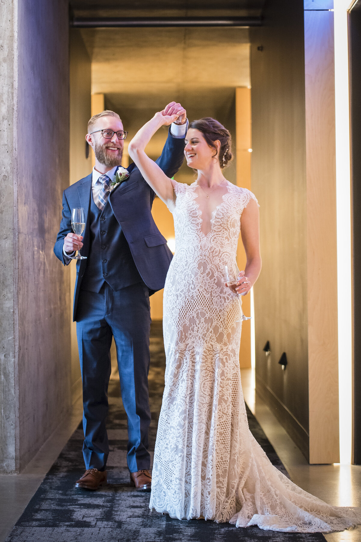 A groom twirls his bride as they hold a flute of champagne in the other hand.