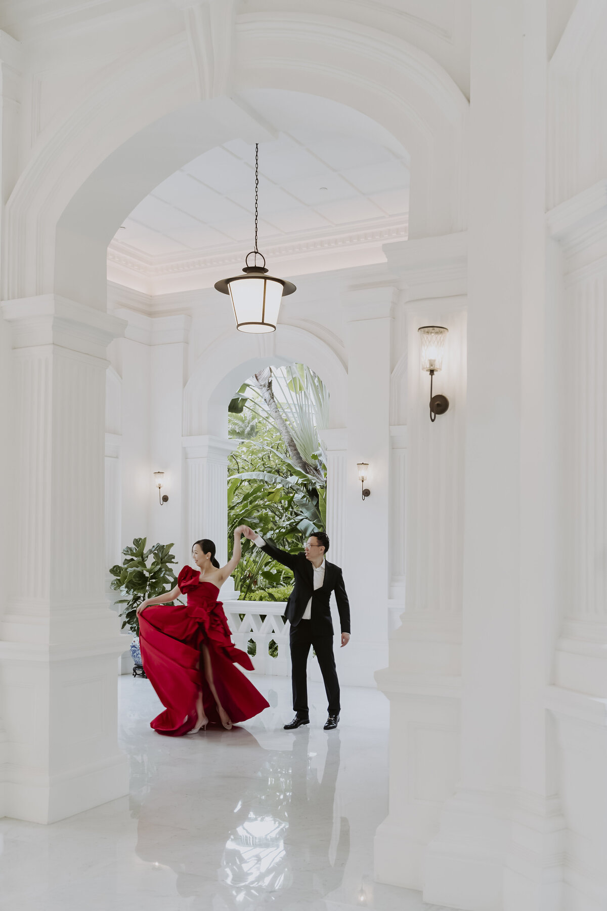 a man in a black suit spins a woman in a red dress in the raffles hotel