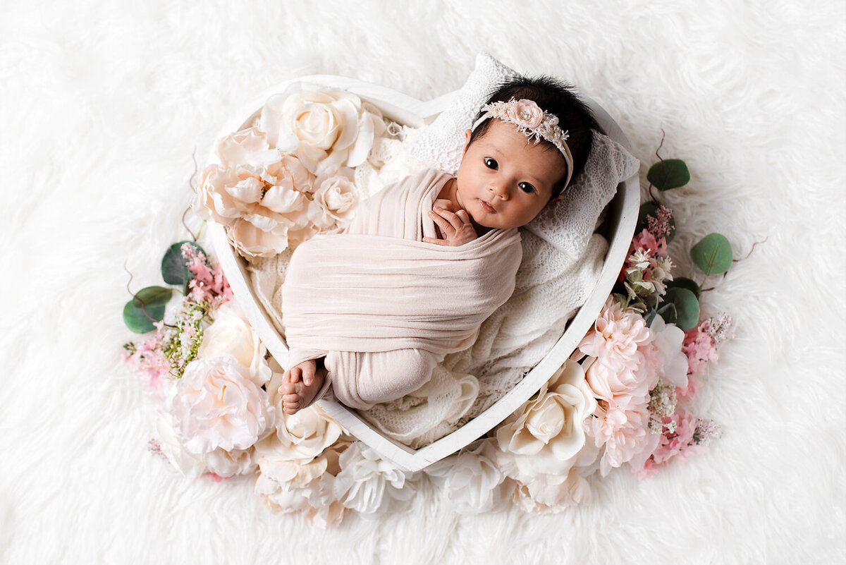 Newborn baby girl with eyes open in heart shape prop.