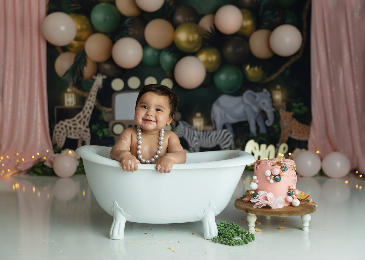 A cake covered one year old girl sits in a bathtub in a studio