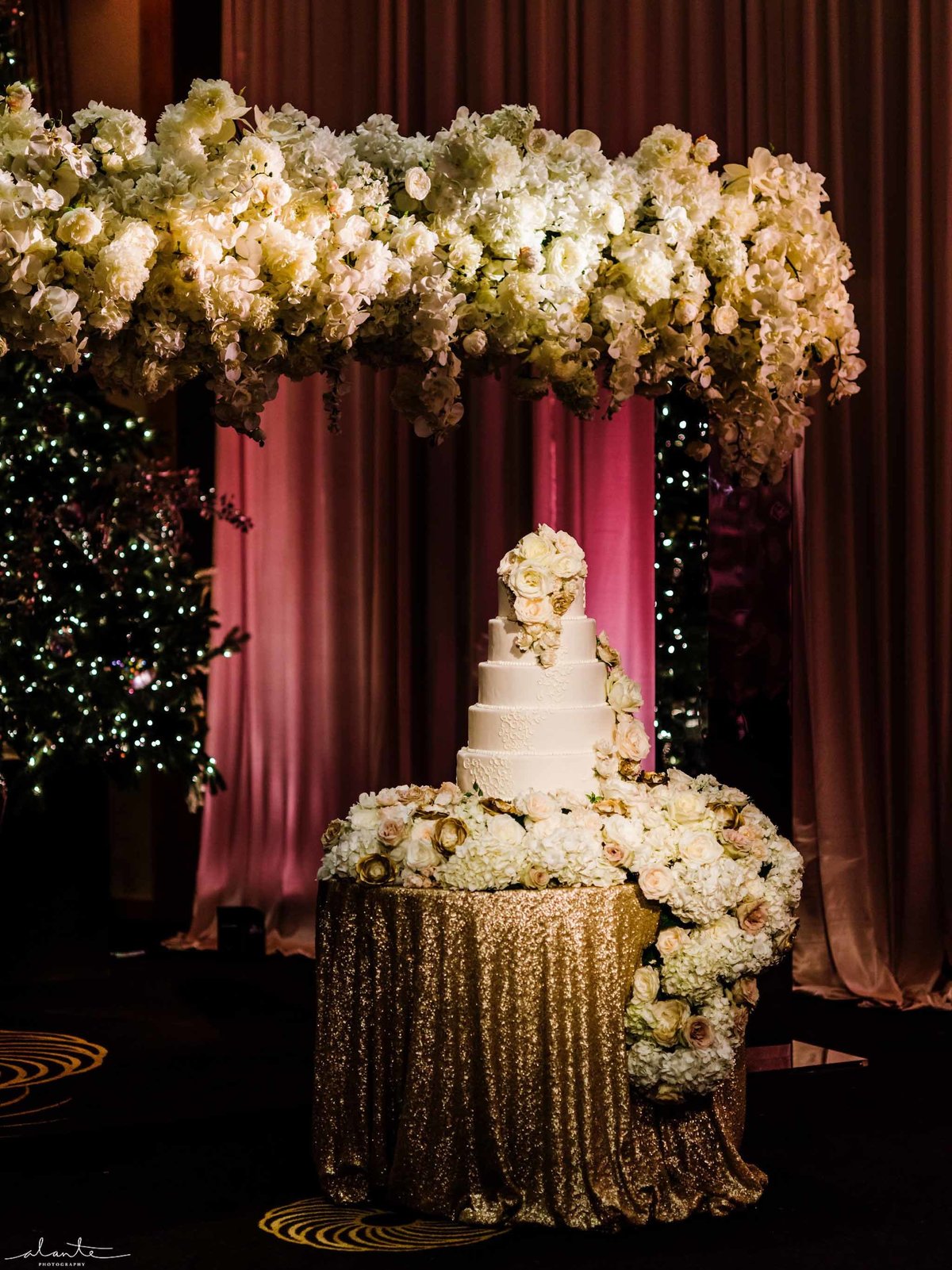 Wedding cake surrounded by white floral cascading over the cake table.