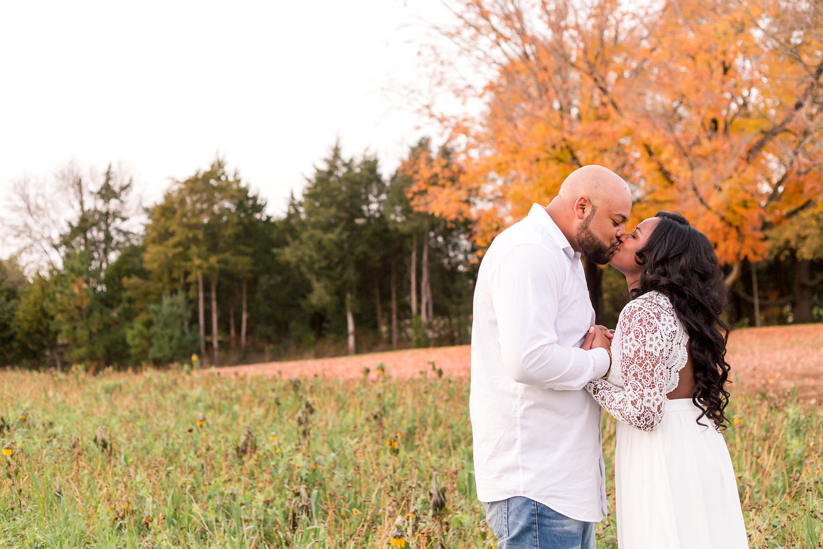 A couple kisses in front of fall leaves at Sneads Asparagus Farm