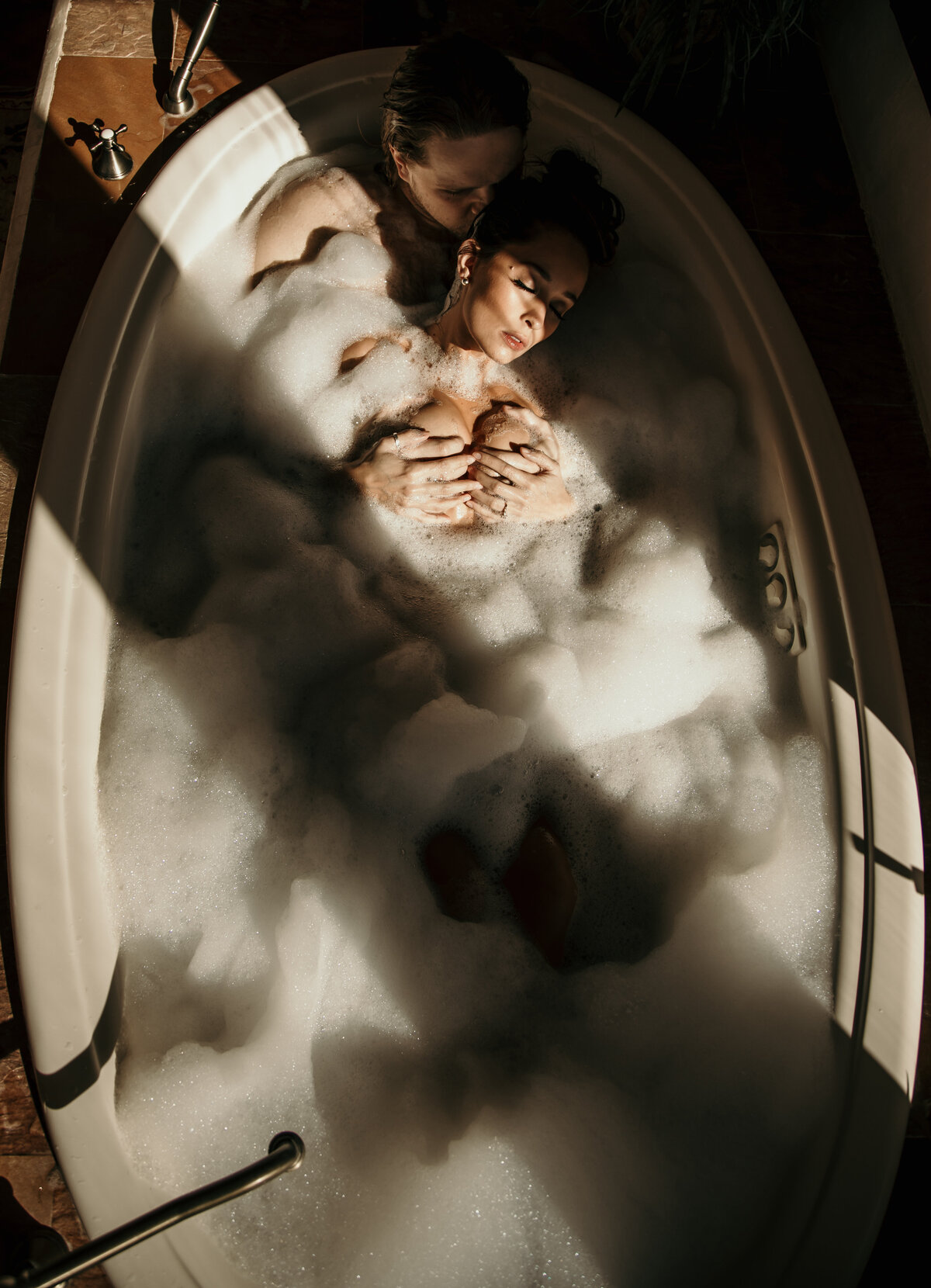 A couple is laying in the bathtub together with bubbles and sunrays