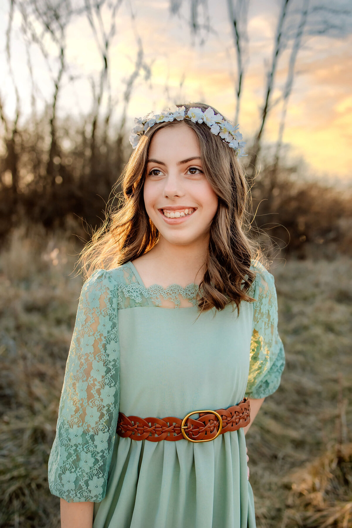 beautiful young lady in a long green dress in a field at sunset