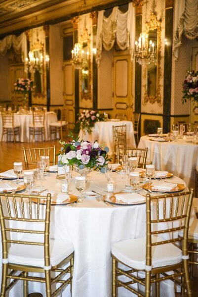 Tables are set for an elegant wedding reception including ornate gold chairs
