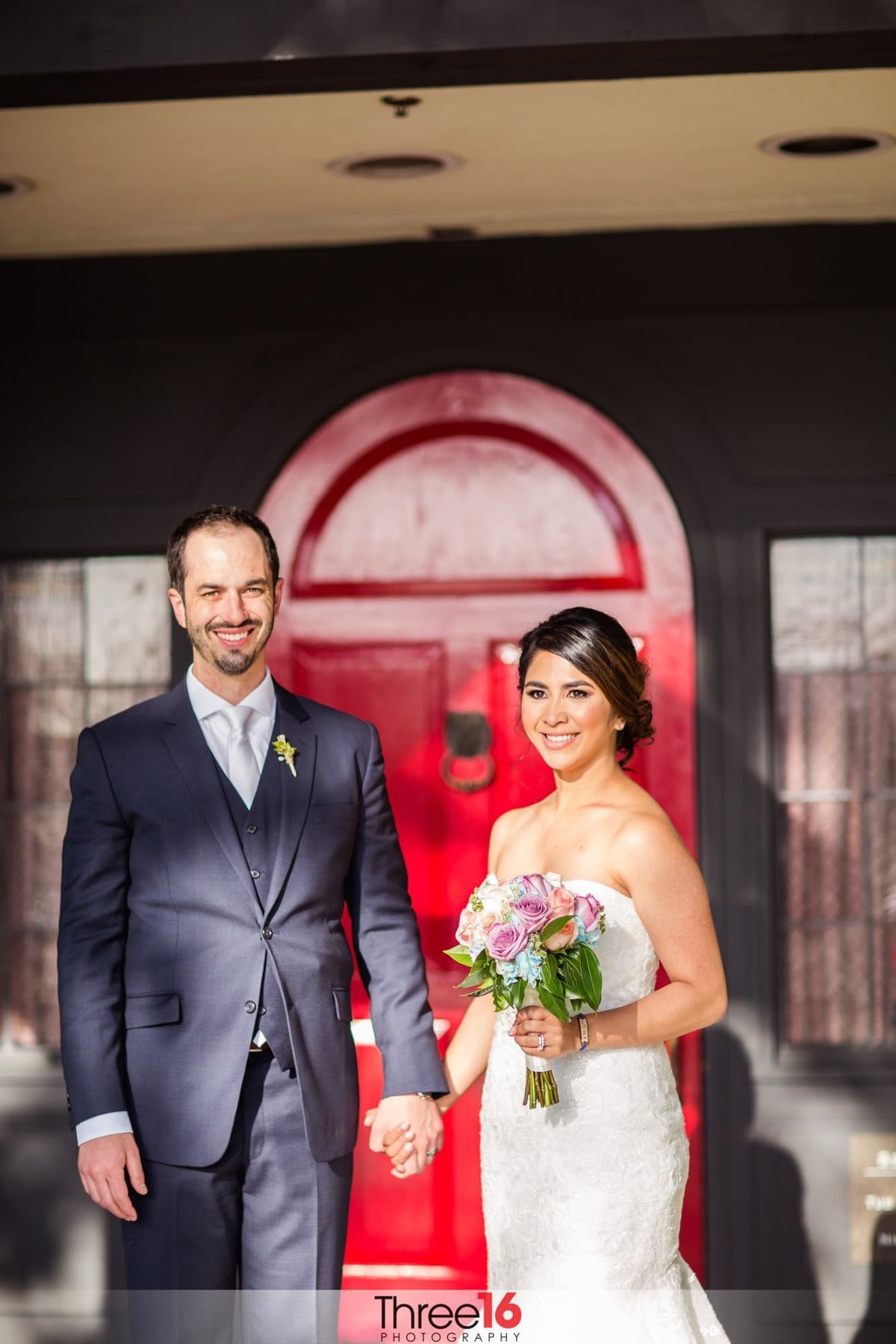 Bride and Groom pose holding hands in front of the red door entrance at the Summit House
