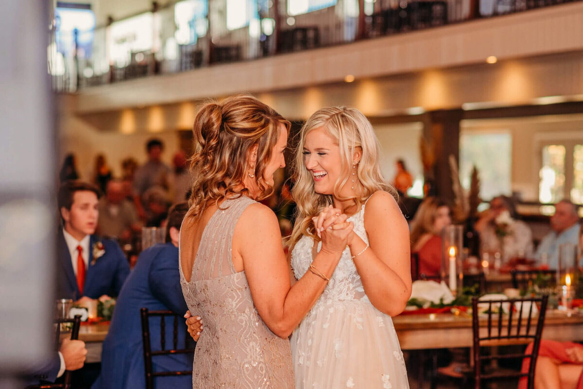 photo of a bride laughing ashy slow dances with her mom at her wedding