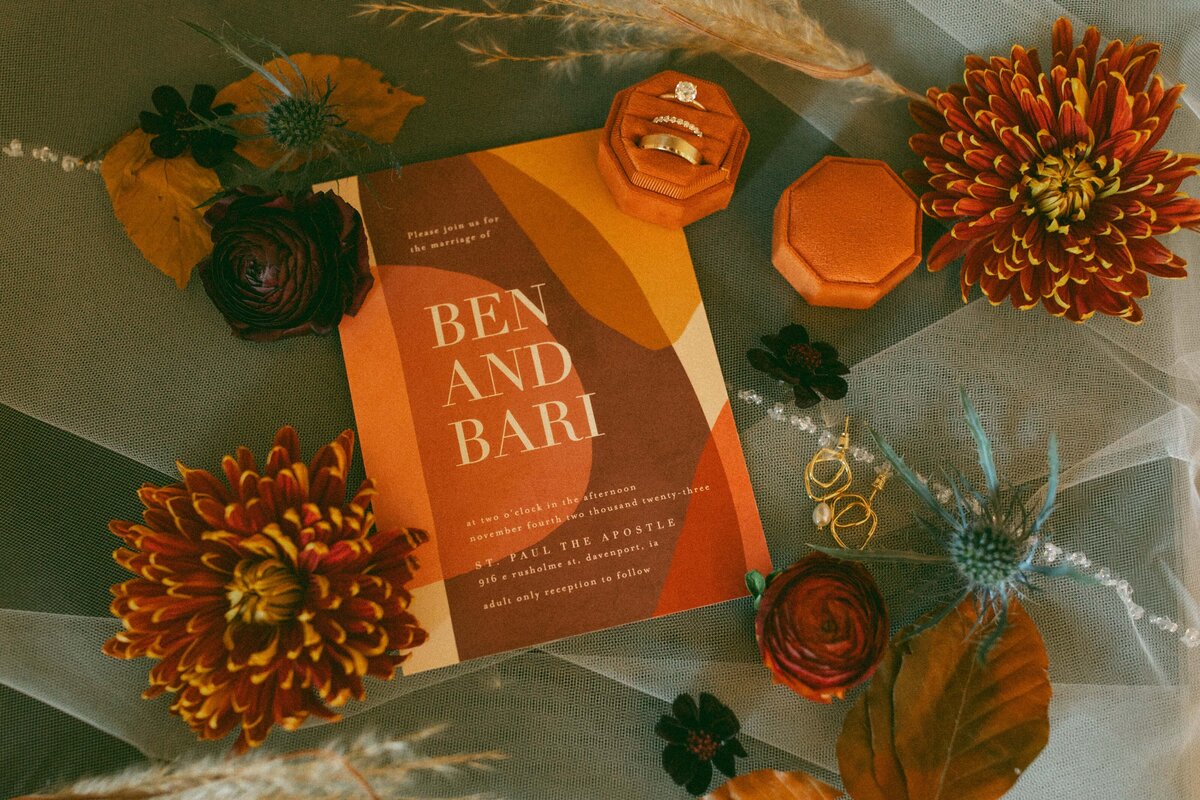 Wedding invitation with names "ben and bari," surrounded by autumn-colored flowers, a veil, and wedding rings on a textured background, perfect for park farm winery weddings.