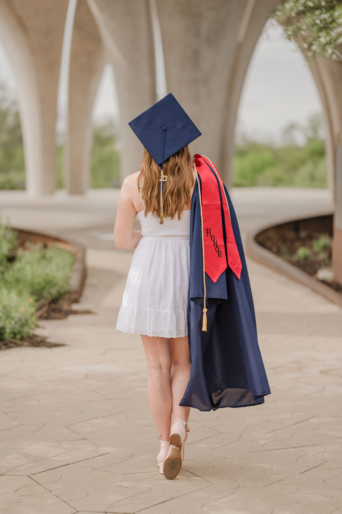 Graduation picture of a San Antonio girl wearing her cap and holding her gown over her shoulder as she walks away from the camera.
