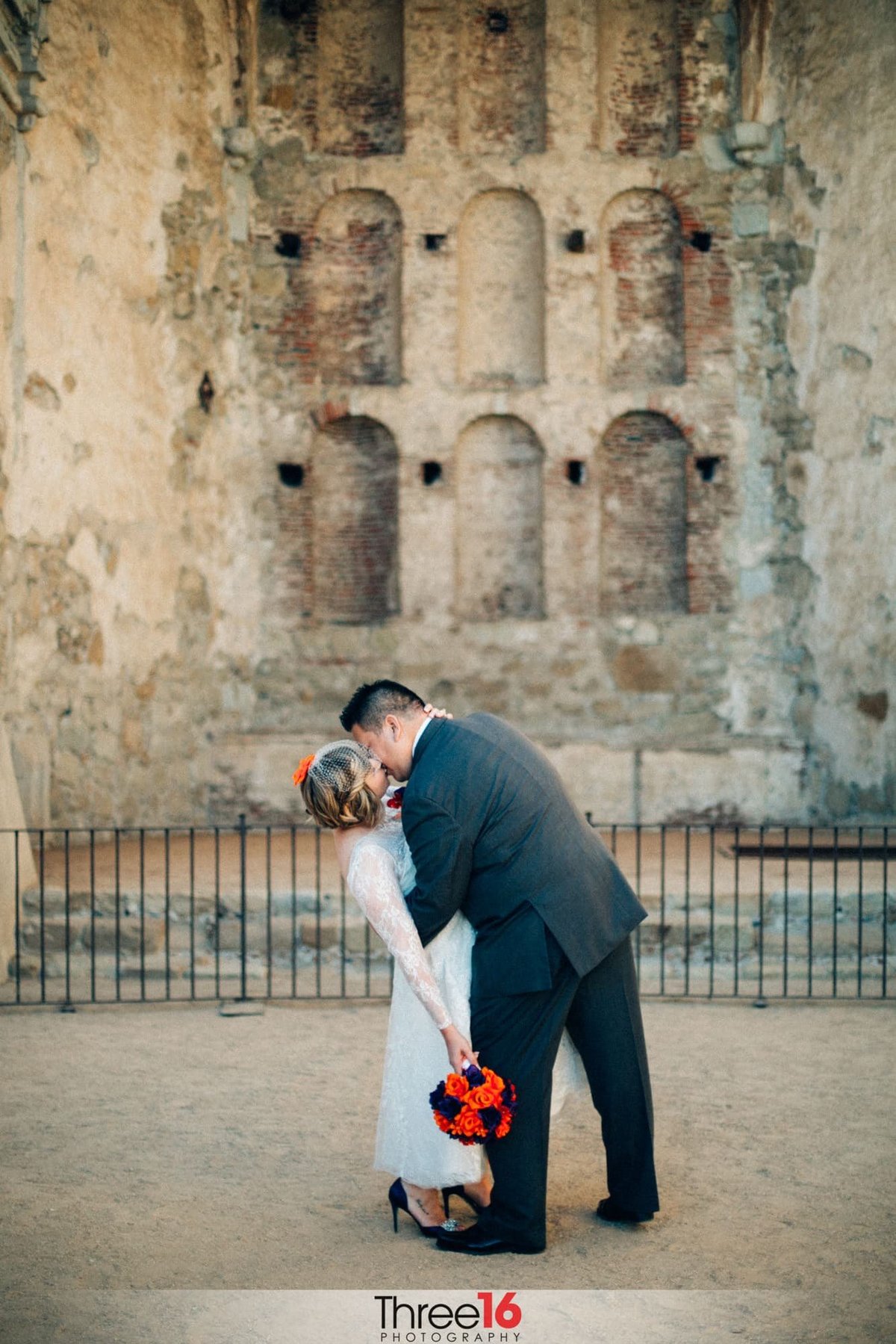 Groom dips his Bride as he kisses her at the Mission San Juan Capistrano