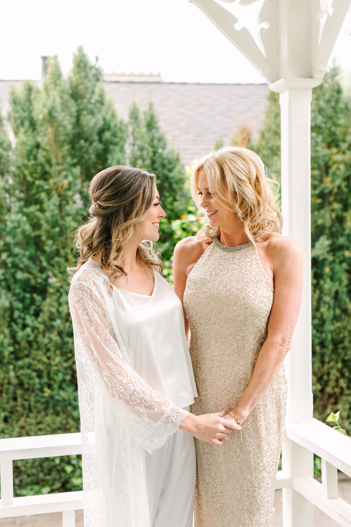 mother of the bride and bride holding hands and smiling at each other on a sunny patio in napa.