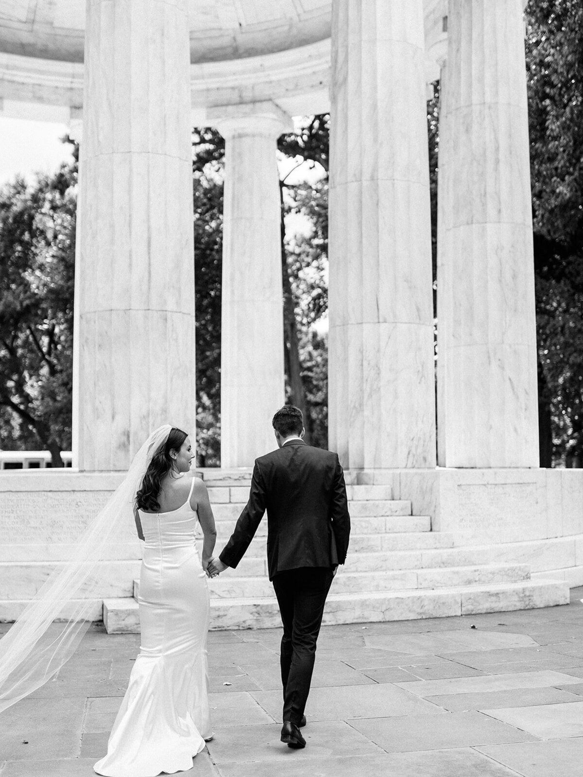 couple walking towards dc war memorial as they hold hands.