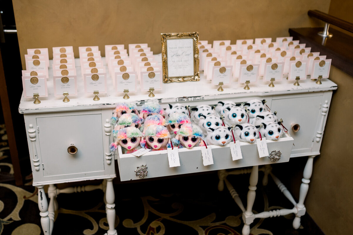 Escort card table display on a white buffet cabinet for a 50th anniversary celebration, featuring wax seal adorned place cards. The drawer below holds Beanie Babies as playful placeholders for kids’ place cards, adding a charming touch to the event at The Northern Hotel in Billings, MT.