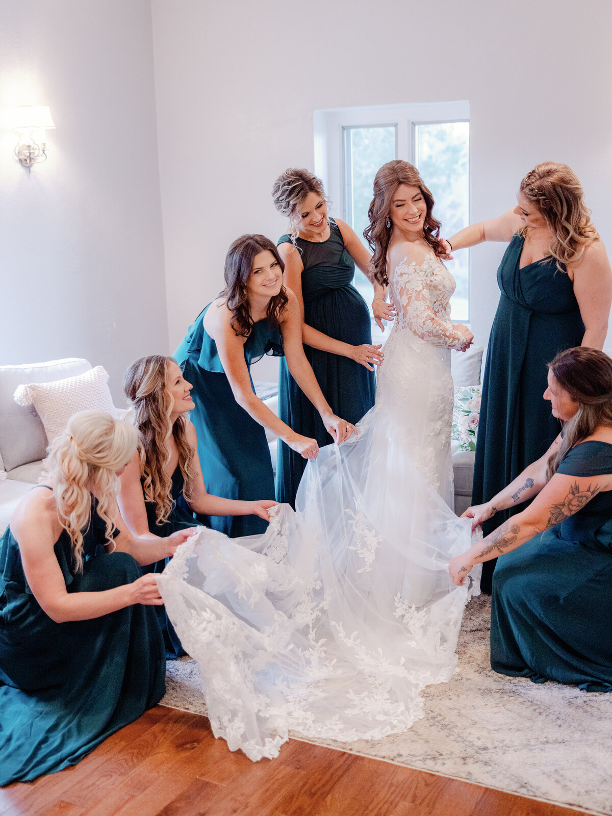 Bridesmaids dressed in dark teal dresses help the bride with her finishing touches before they all head to the wedding ceremony