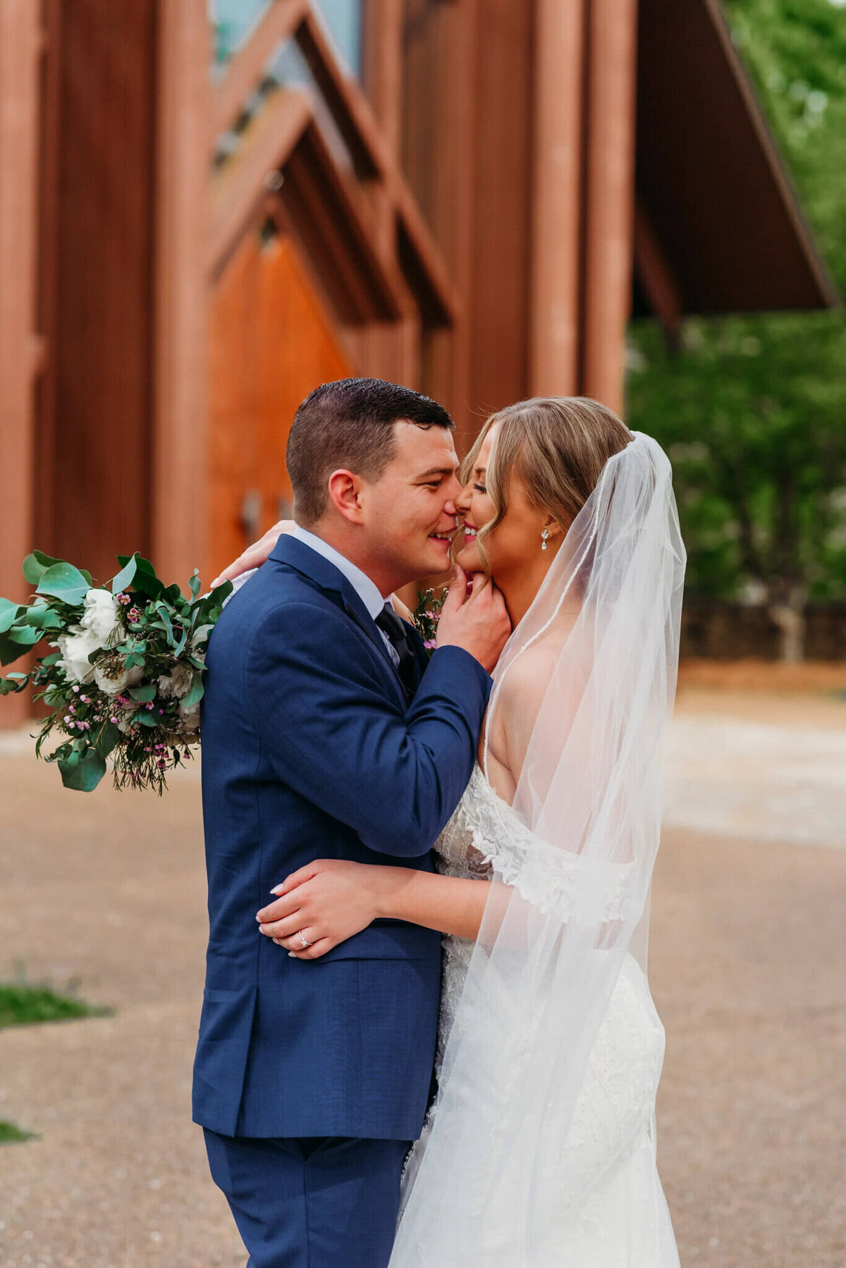 photo of a bride and groom kissing while standing in front of a wooden wedding chapel