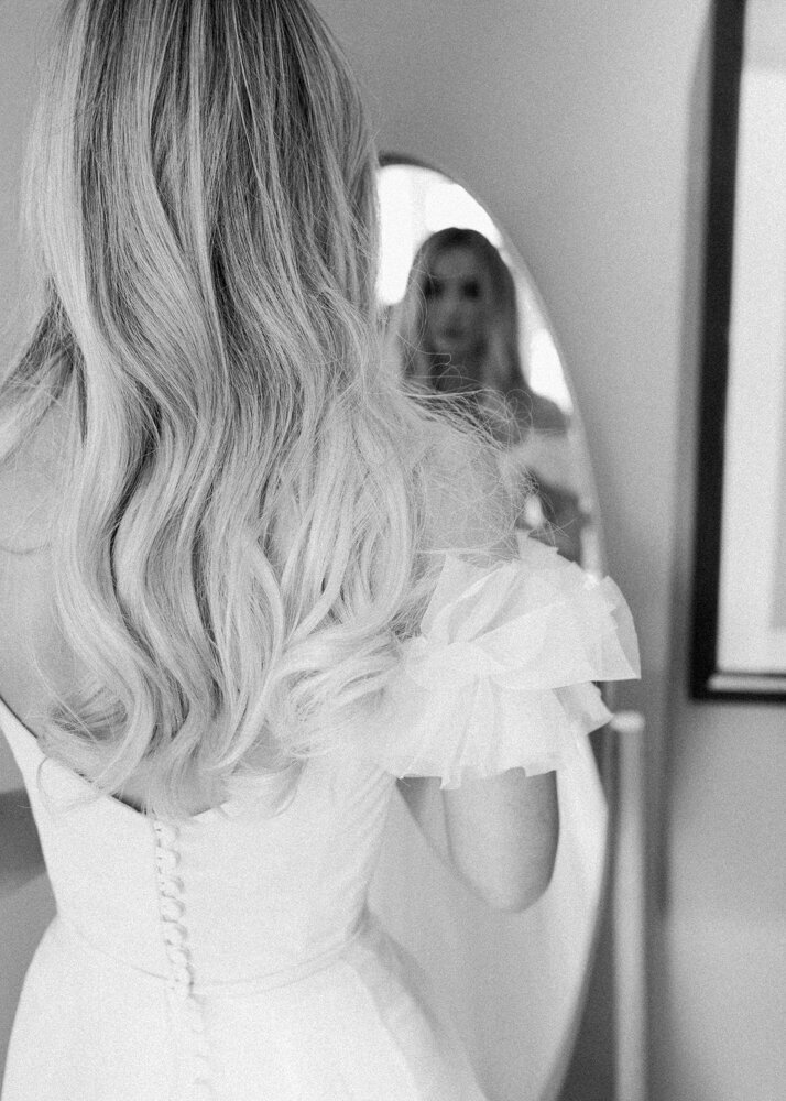 bride wearing wedding dress looking in the mirror captured