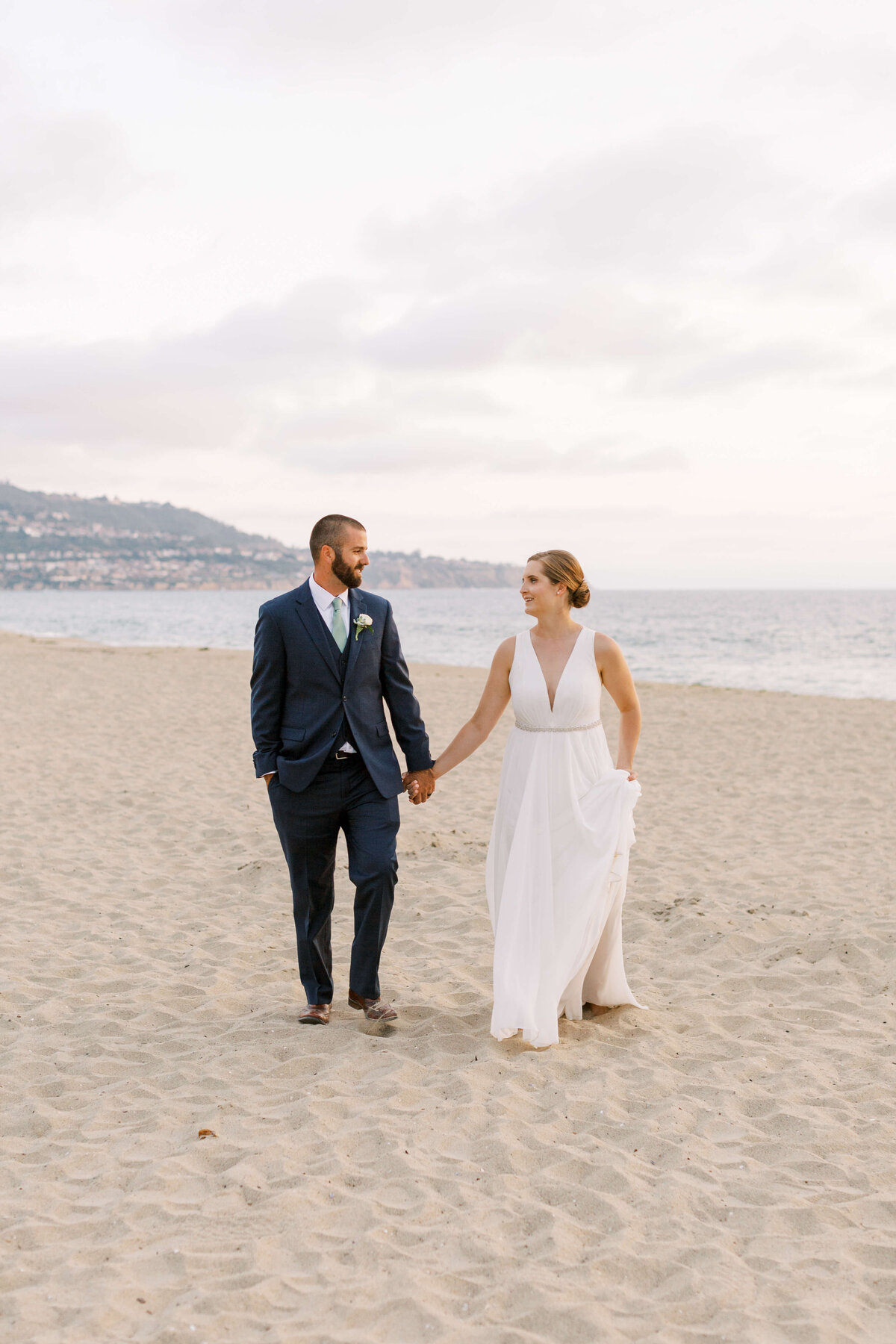 Bride and groom walk hand in hand down the beach in Southern California after celebrating their wedding day together