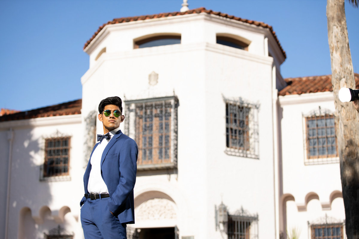 Senior boy in blue suite with sunglasses infront of white building.