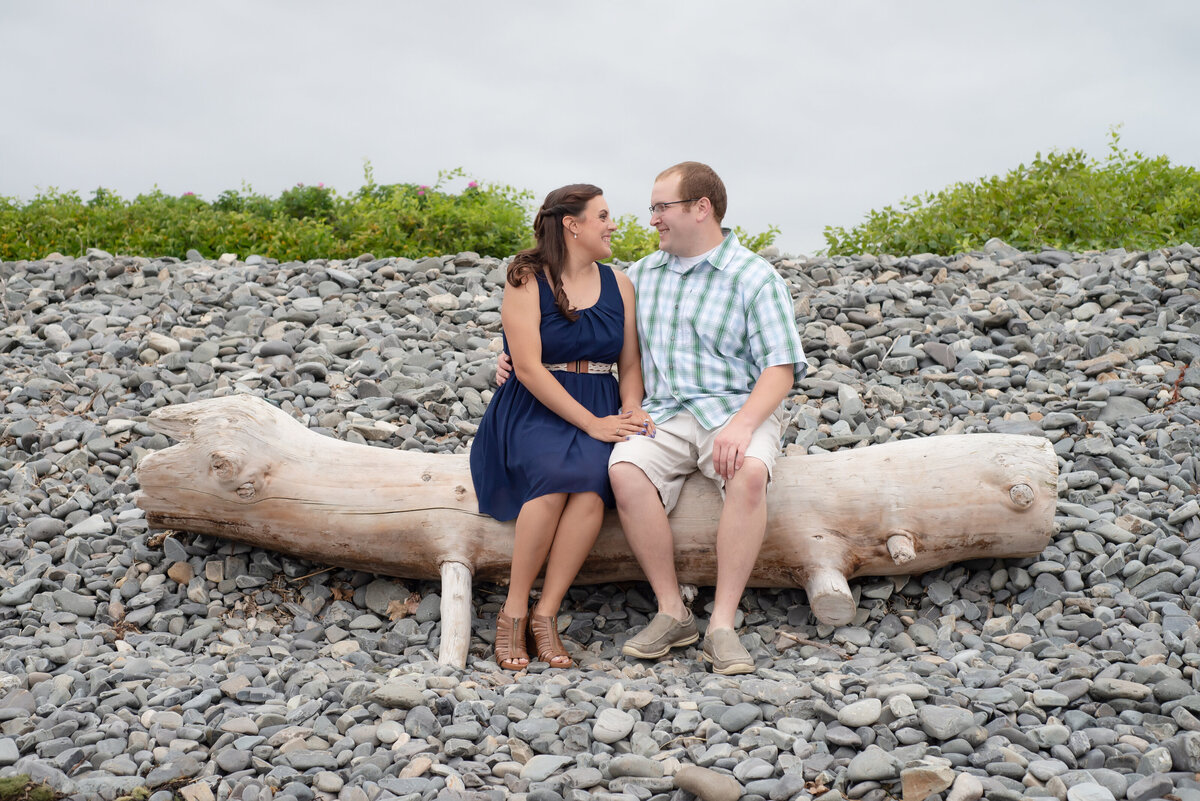Engaged couple sitting on driftwood in York, Maine