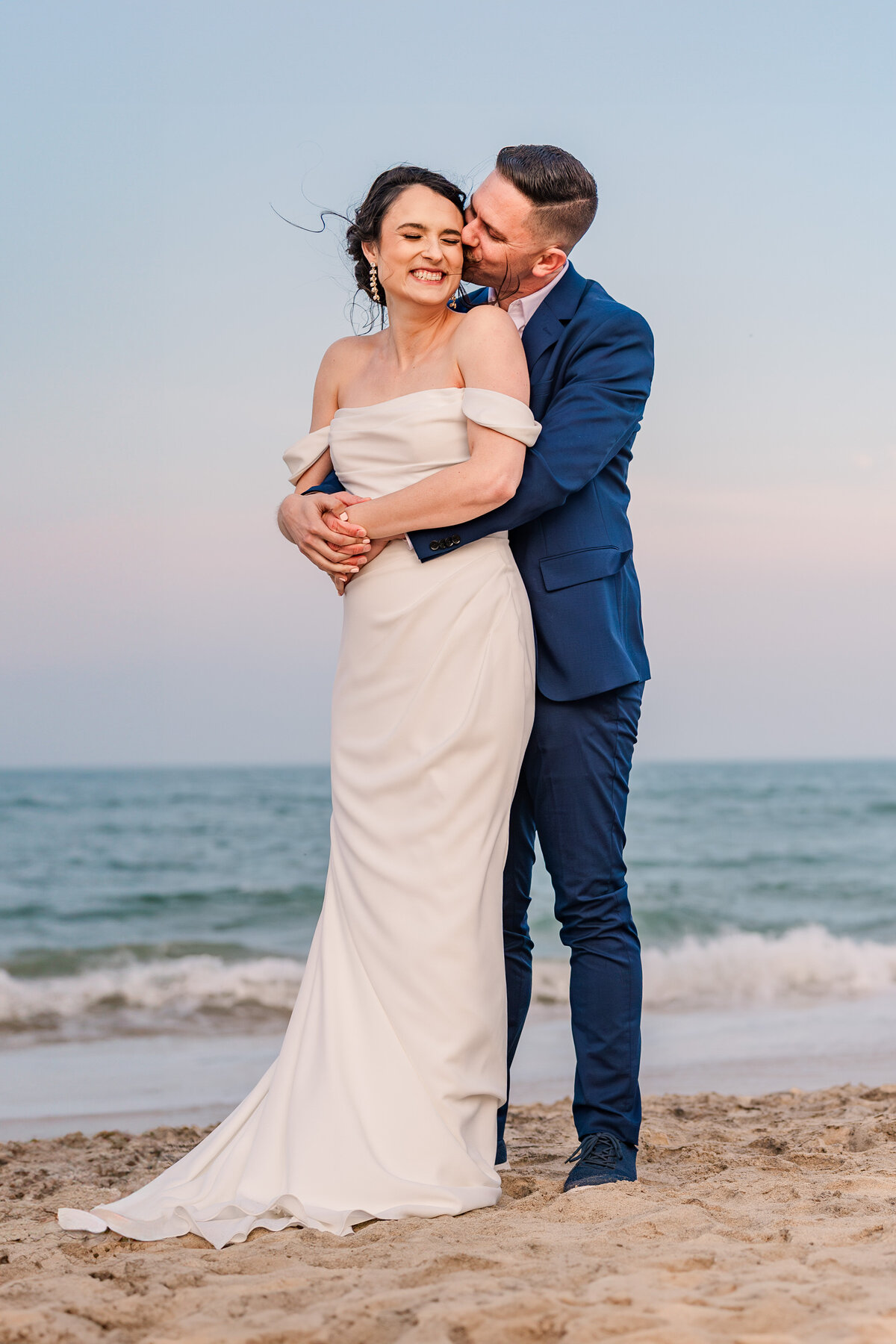 A married couple hugging and kissing at sunset at Wrightsville Beach at sunset by JoLynn Photography, a Wilmington wedding photographer