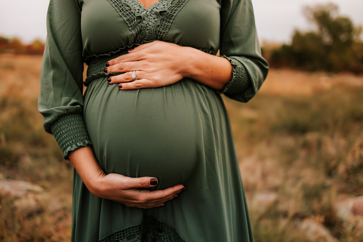 pregnant mom holds belly in a long green dress for maternity photos