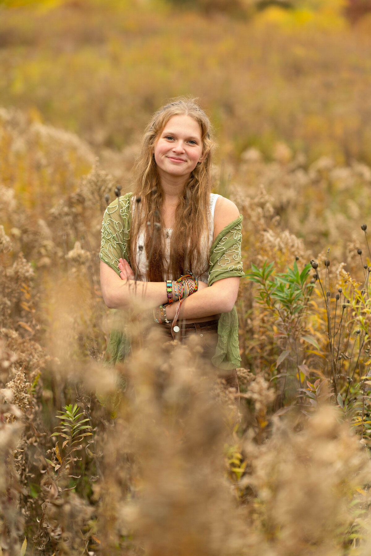 Senior girl stands in wheat field with arms crossed.