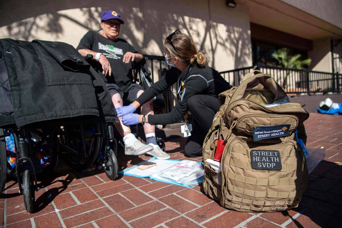 Marketing Shot showing the team in action offering medical care to a homeless women in wheelchair with a leg injury.