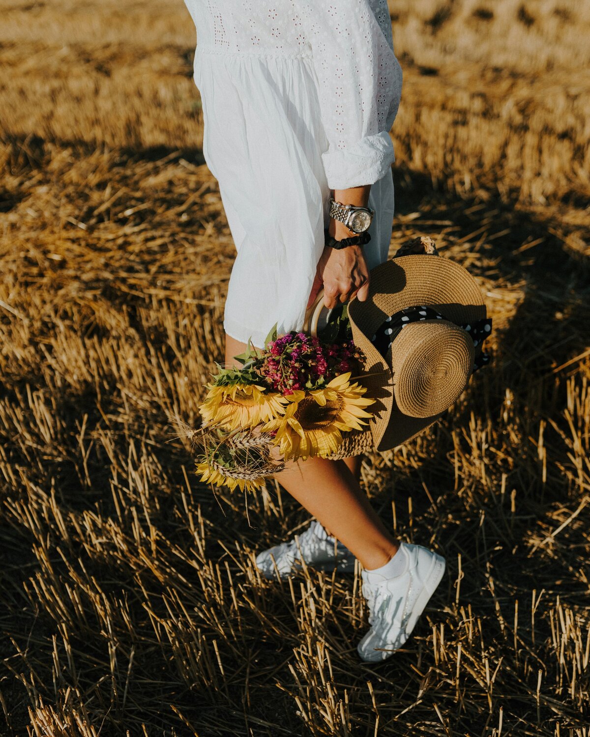 girl in white trainers walking in field with sunflwer in basket
