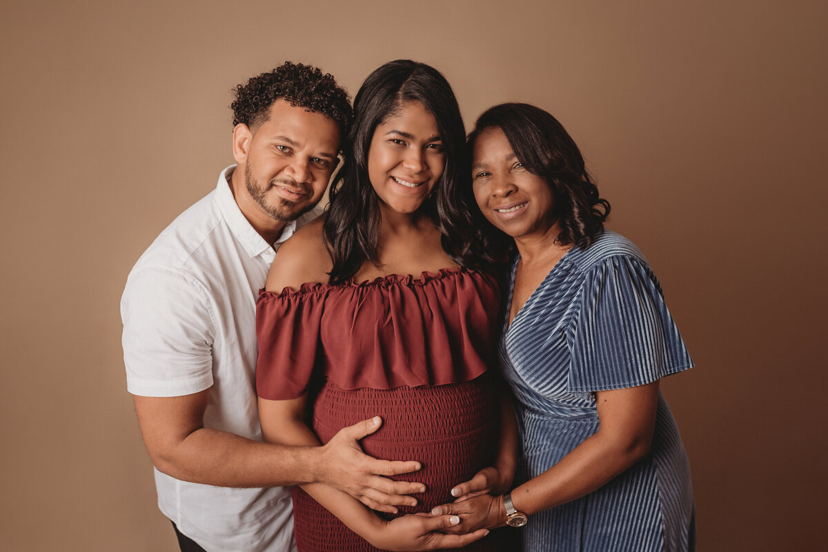 Husband and wife with wife's mom posing for maternity portraits wearing white, burgundy and blue outfits / gowns.