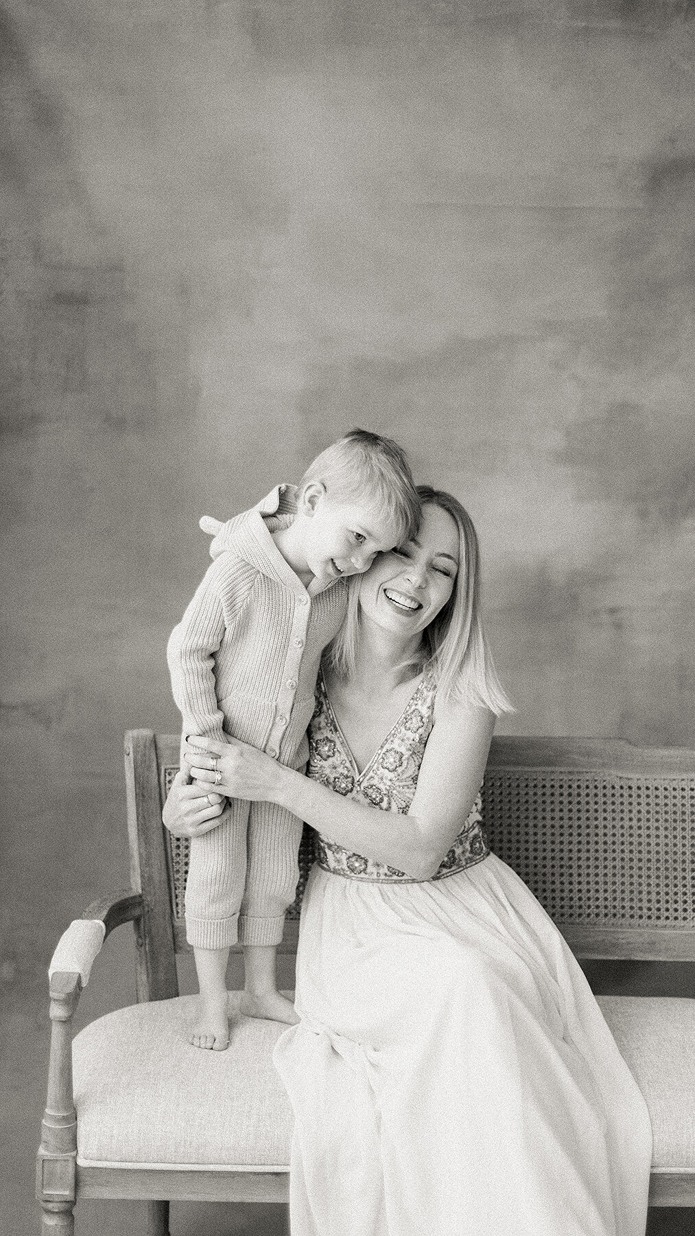 A beautiful black and white portrait of a mother sitting on a chair in a Dallas photography studio all snuggled up with her son.