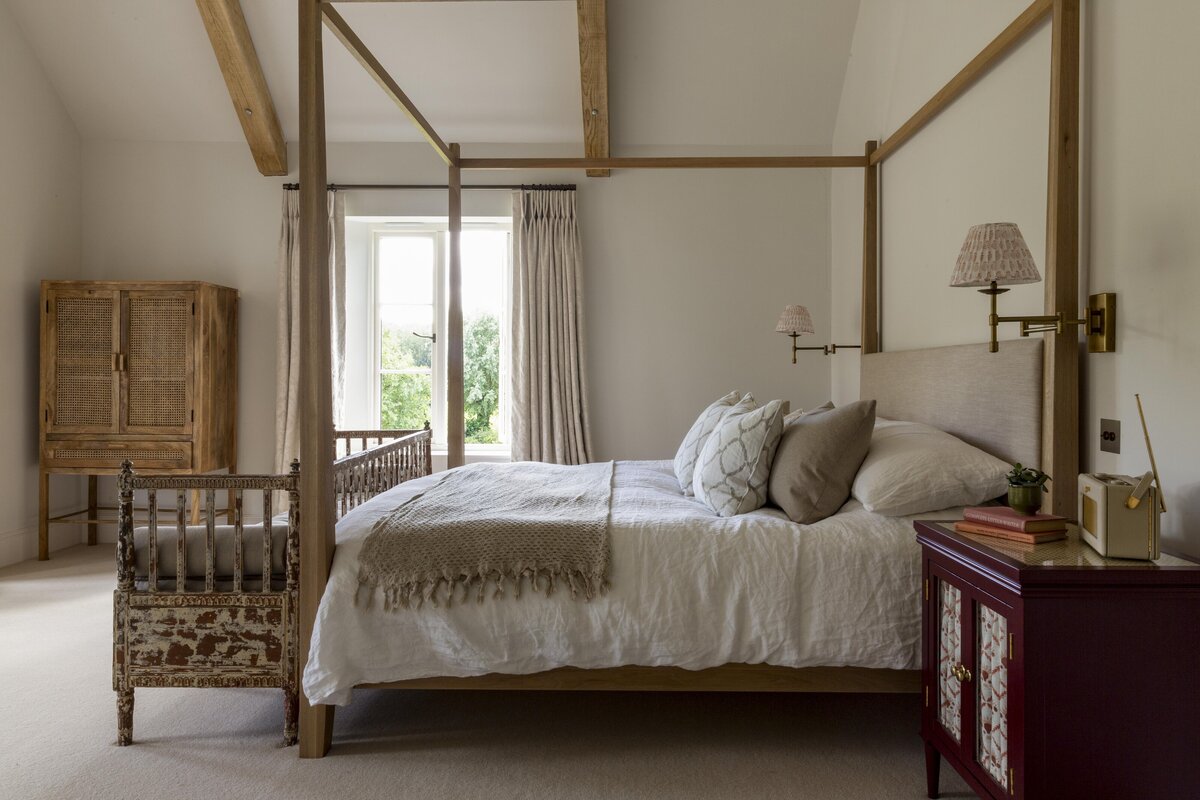 four poster king bed with neutral shades and a red side table