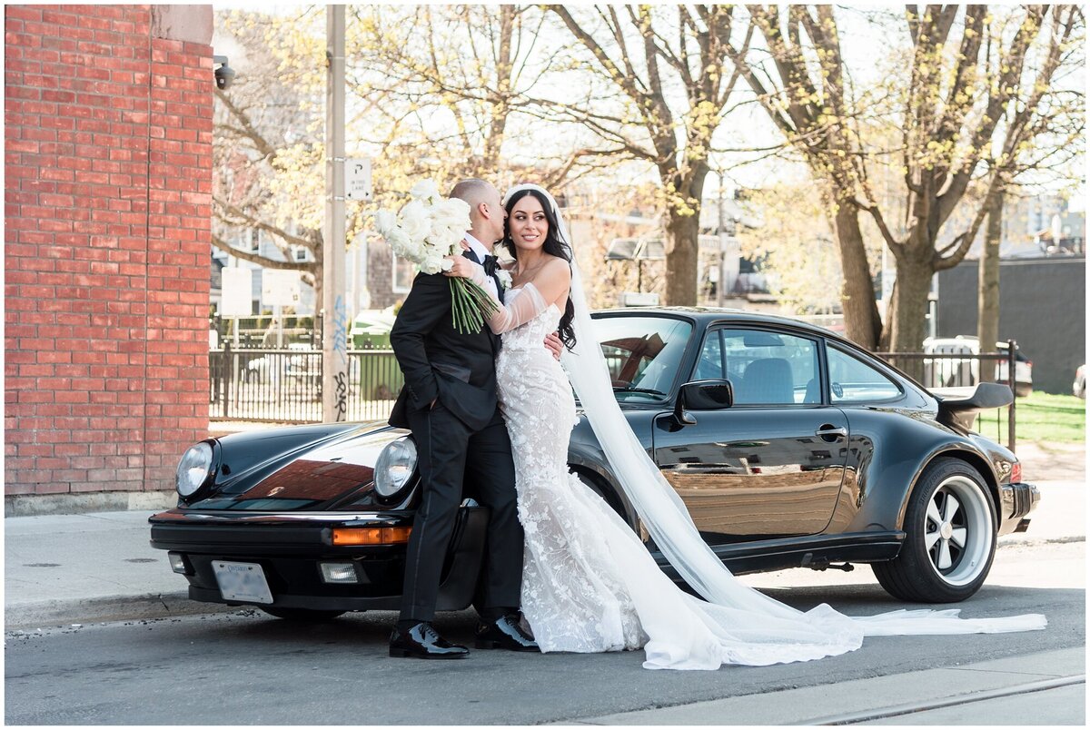 Urban portrait of bride and groom next to a black classic Porsche