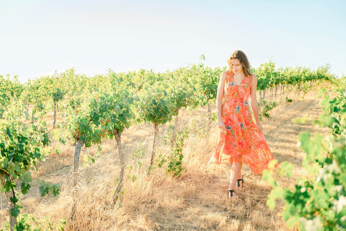 Senior girl in an orange dress walking through Livermore vineyards for her senior pictures with Bay Area photographer Kristen Hazelton