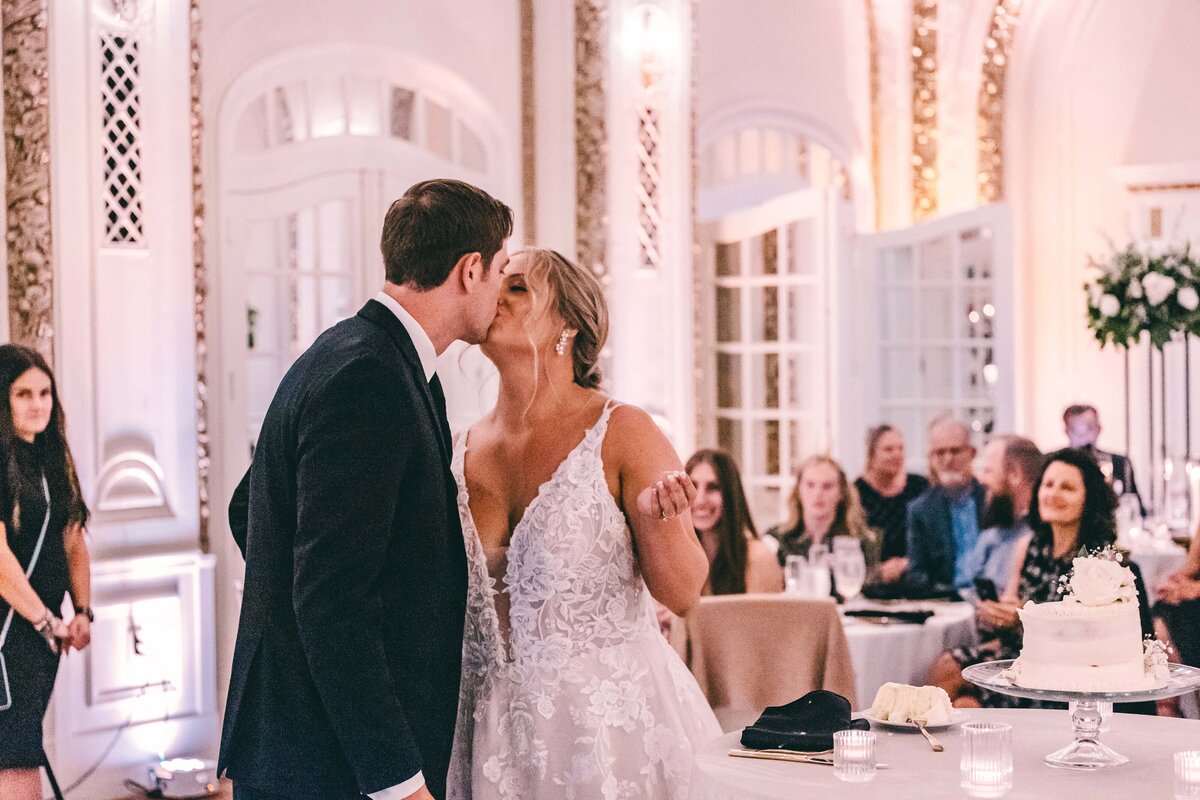 A bride and groom kissing at their wedding reception in Des Moines, surrounded by guests and elegant decor.