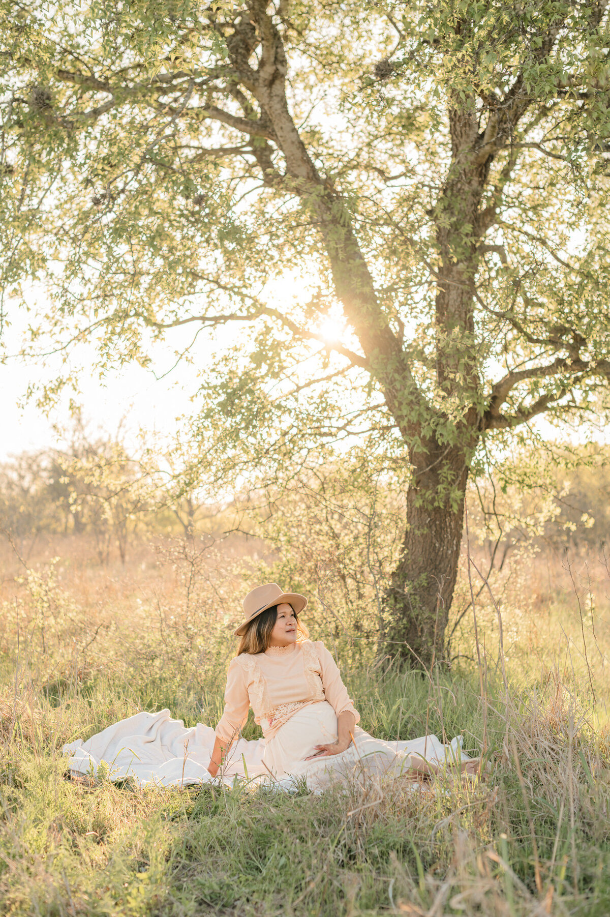 Expecting mom sits on a blanket during golden hour at Crescent Bend Nature Center, by San Antonio maternity photographer Cassey Golden.