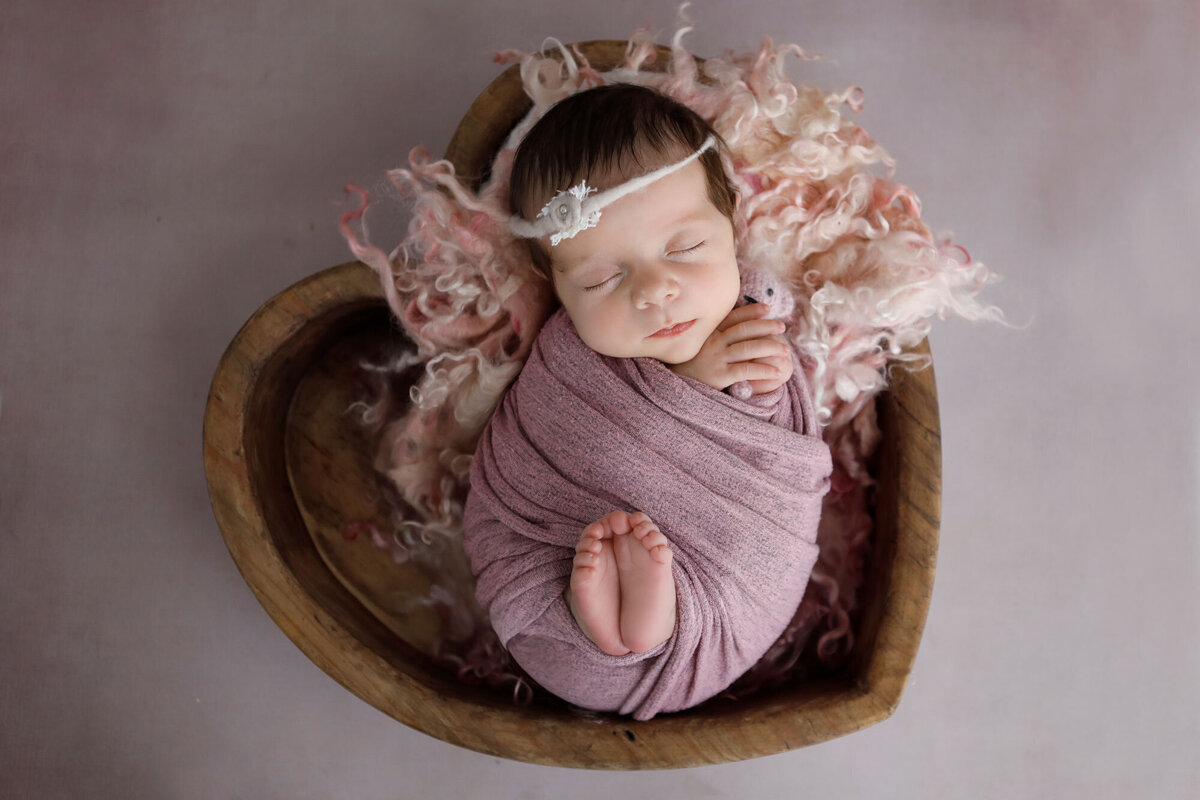newborn-baby-girl-wrapped-in-a-pink-wrap-and-sleeping-in-a-wooden-heart-bowl
