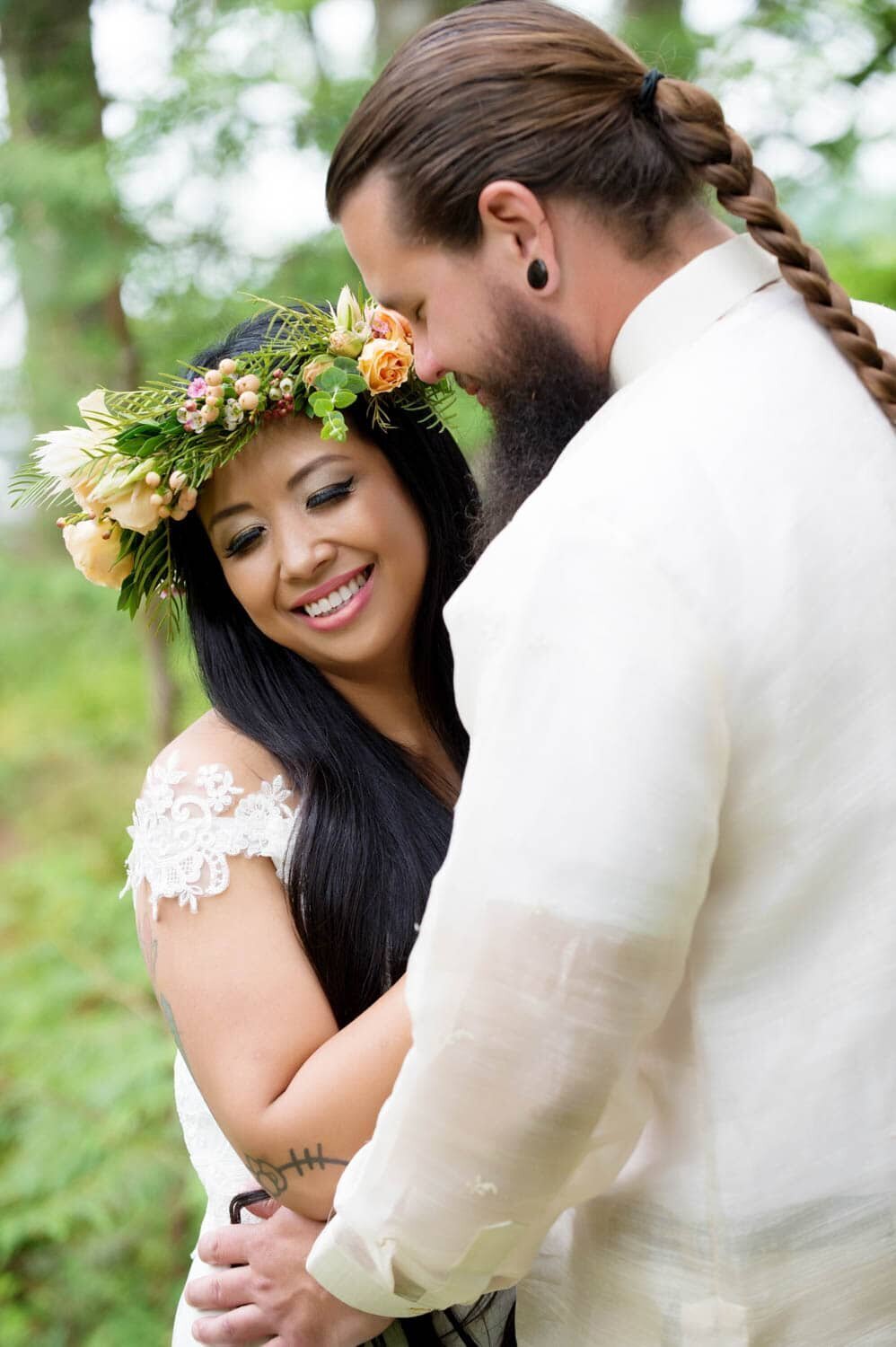 a man with a long braid hugs a bride wearing a colorful floral crown