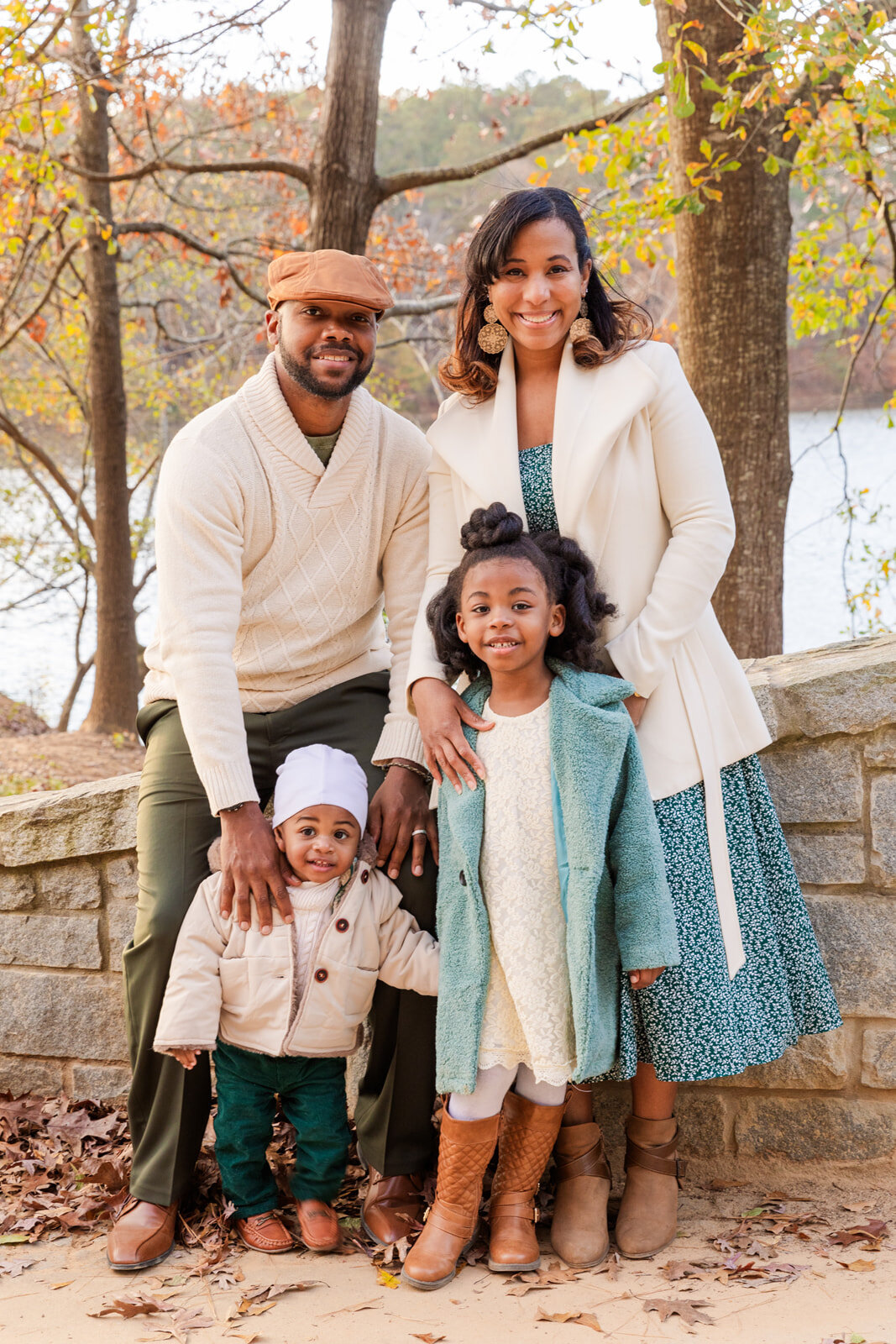 Family of four with young girl and toddler boy standing on a bridge during winter photo session wearing coordiated white and green outfits by Laure photography
