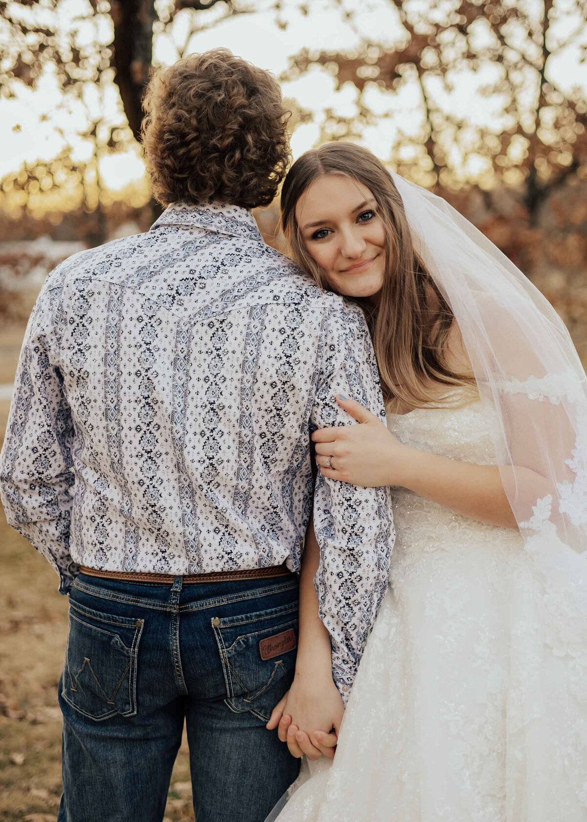Maddie Rae Photography bride and groom standing side by side holding hands. he is facing away and she is facing the camera smiling. she is holding his arm with her other hand