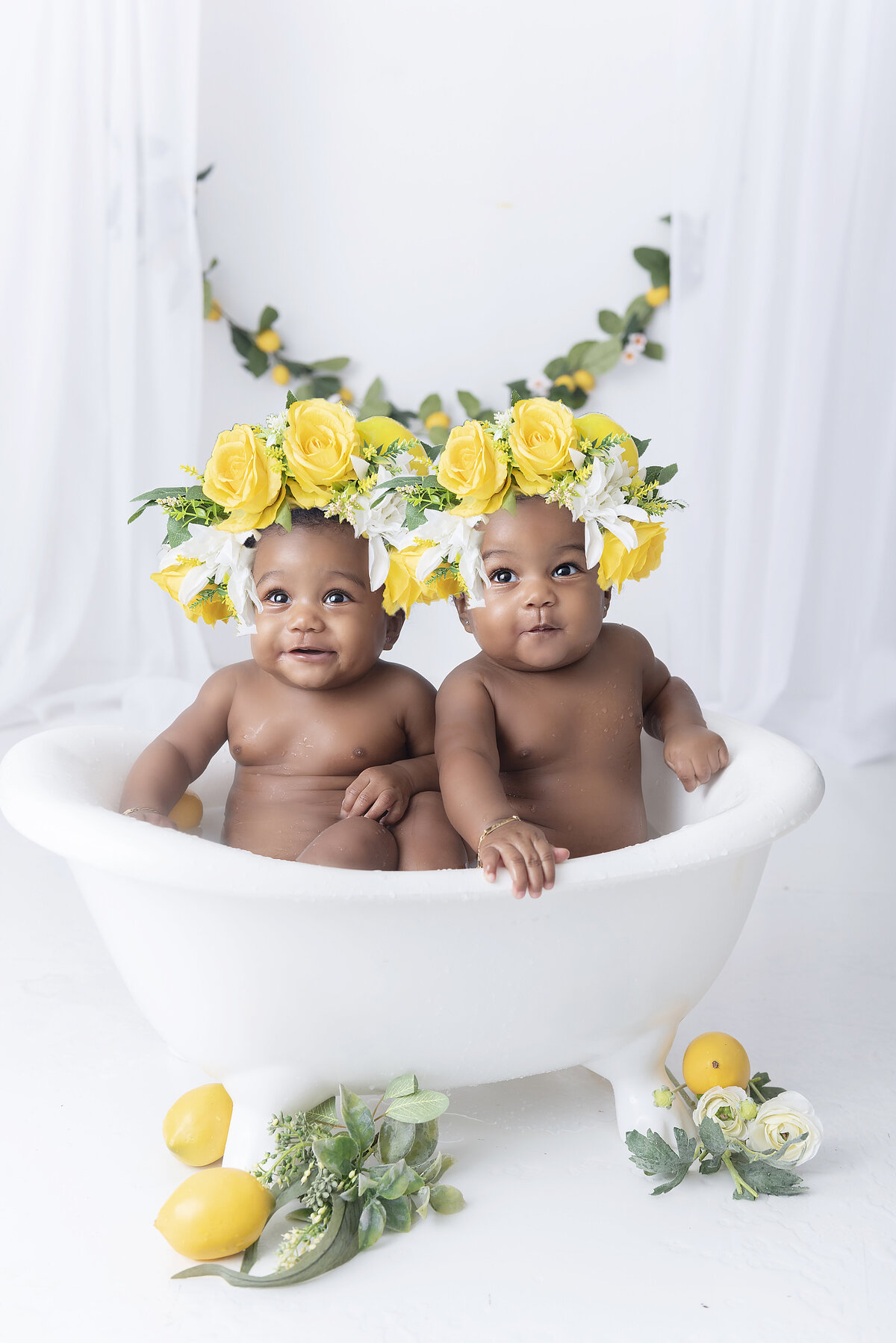 Twin girls sit in a bathrub in yellow floral headbands