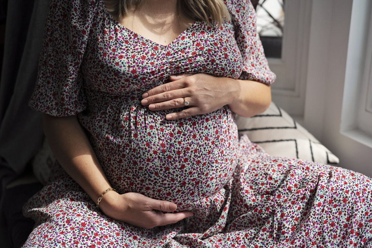 Close up of pregnant lady holding bump wearing a flowery dress during maternity photo shoot