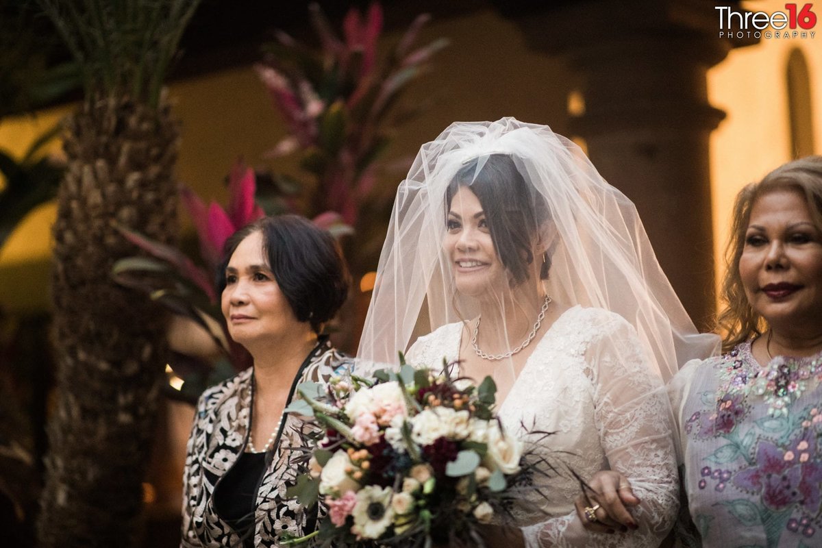 Bride smiles as she is escorted up the aisle by her family
