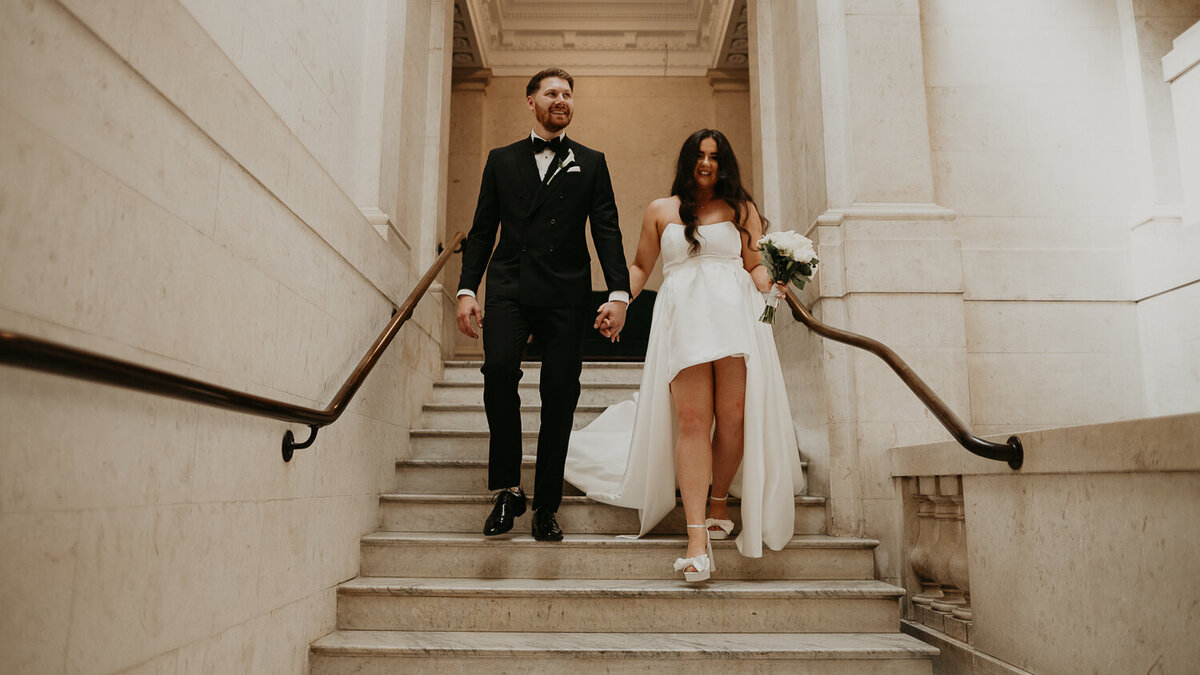 Bride and Groom walk down the stairs at The Old Marylebone Town Hall after their ceremony. 