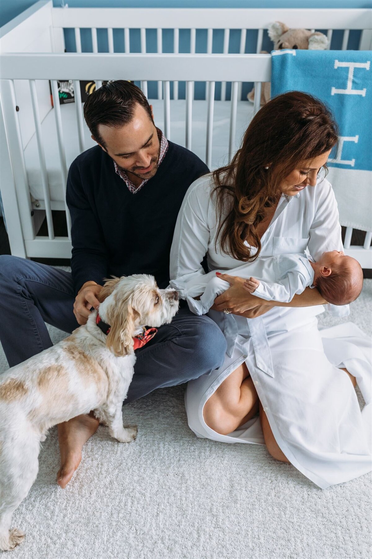 Newborn Photographer, mom holds baby, dad pets dog in nursery
