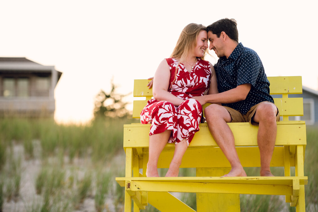 A man and woman sitting on a yellow bench at the beach.