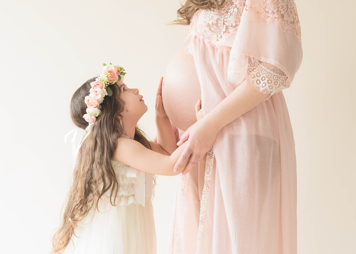 little girl with moms belly bump light and airy soft blush  pink and  cream with a cream backdrop, daughter is wearing flower crown