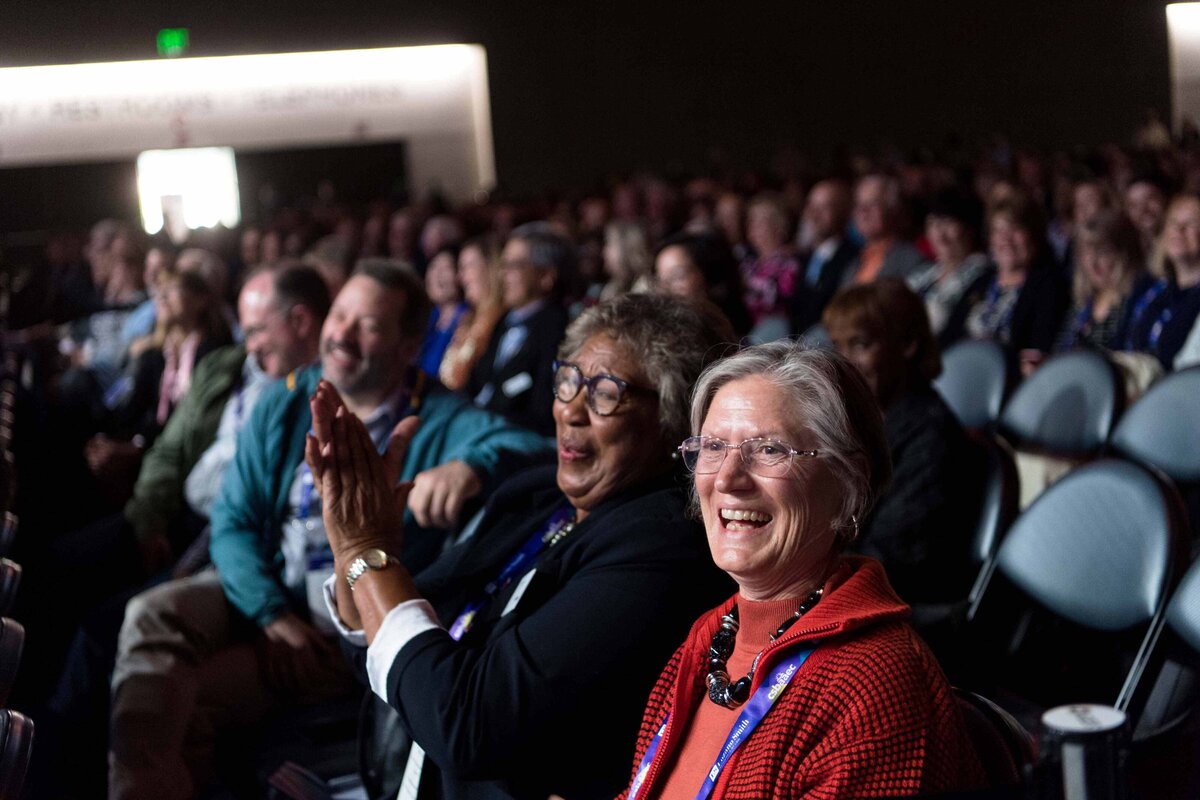 Two women laugh and applaud while seated in the Ballroom at the San Diego Convention Center