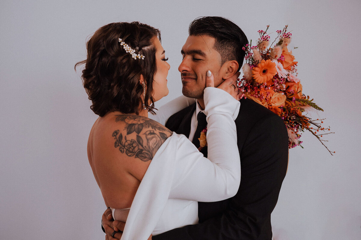 Bride in off the shoulder dress being hugged by groom while bride holds grooms face