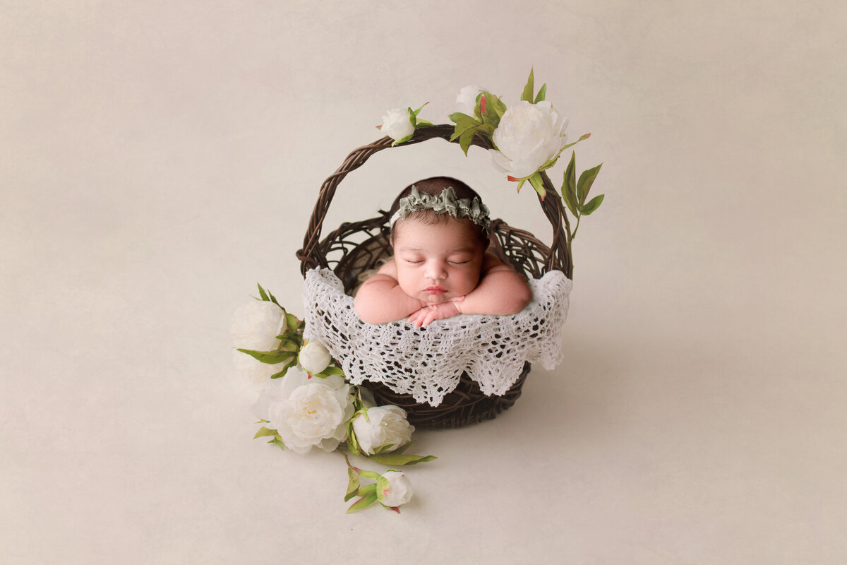 baby girl in a dark wooden basket with  white peonies around